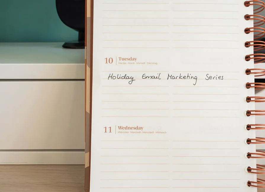 Planner open on a desk with handwritten 'Holiday Email Marketing Series' note.