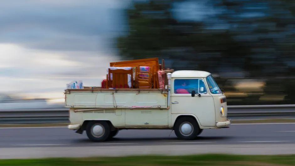 A vintage van loaded with furniture speeding down a highway, showcasing motion and travel.